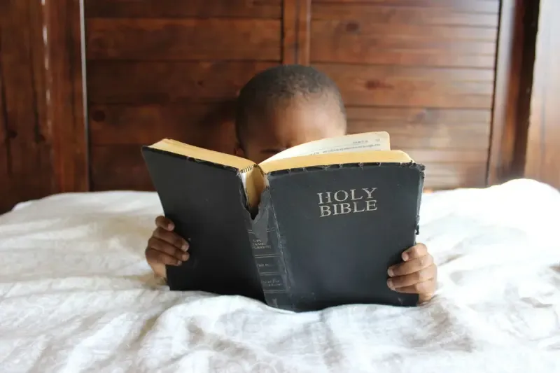 bible study showing a baby boy with a large bible covering his face and reading it