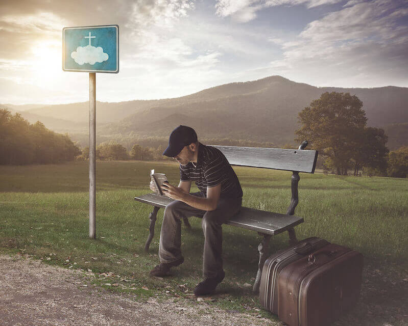 A man waiting at a bus stop reading the Bible