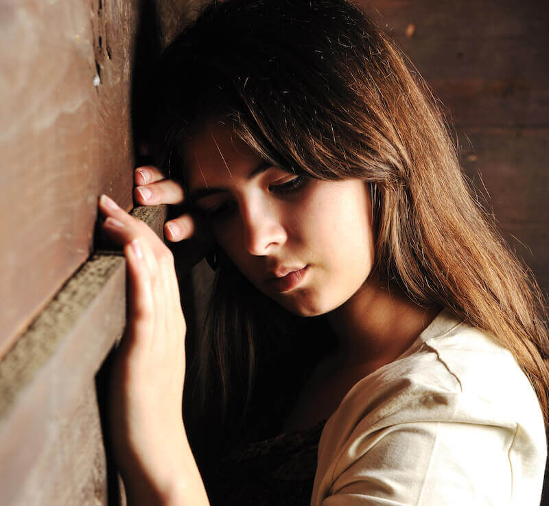 Shame image showing a woman learning on the wall in shame