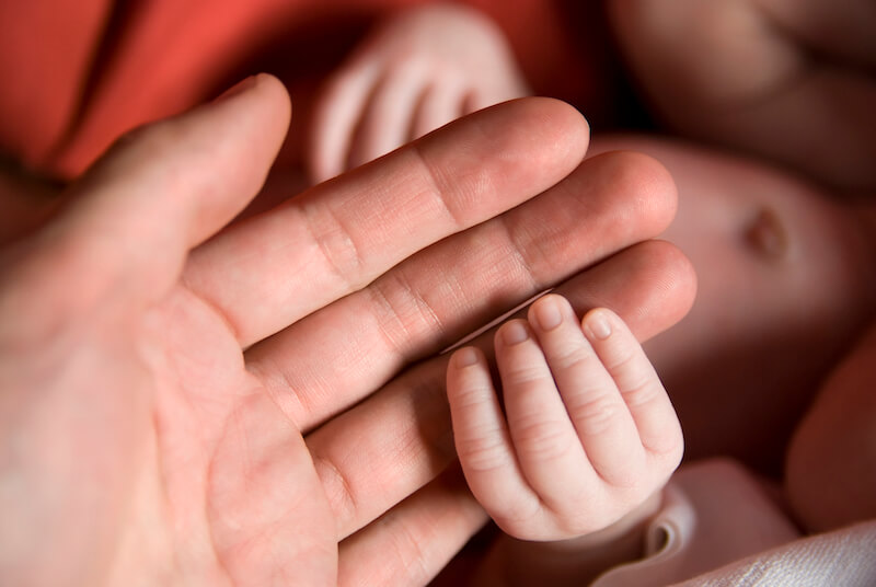 God's first breath as a man showing the hands of a newborn holding the father's hands